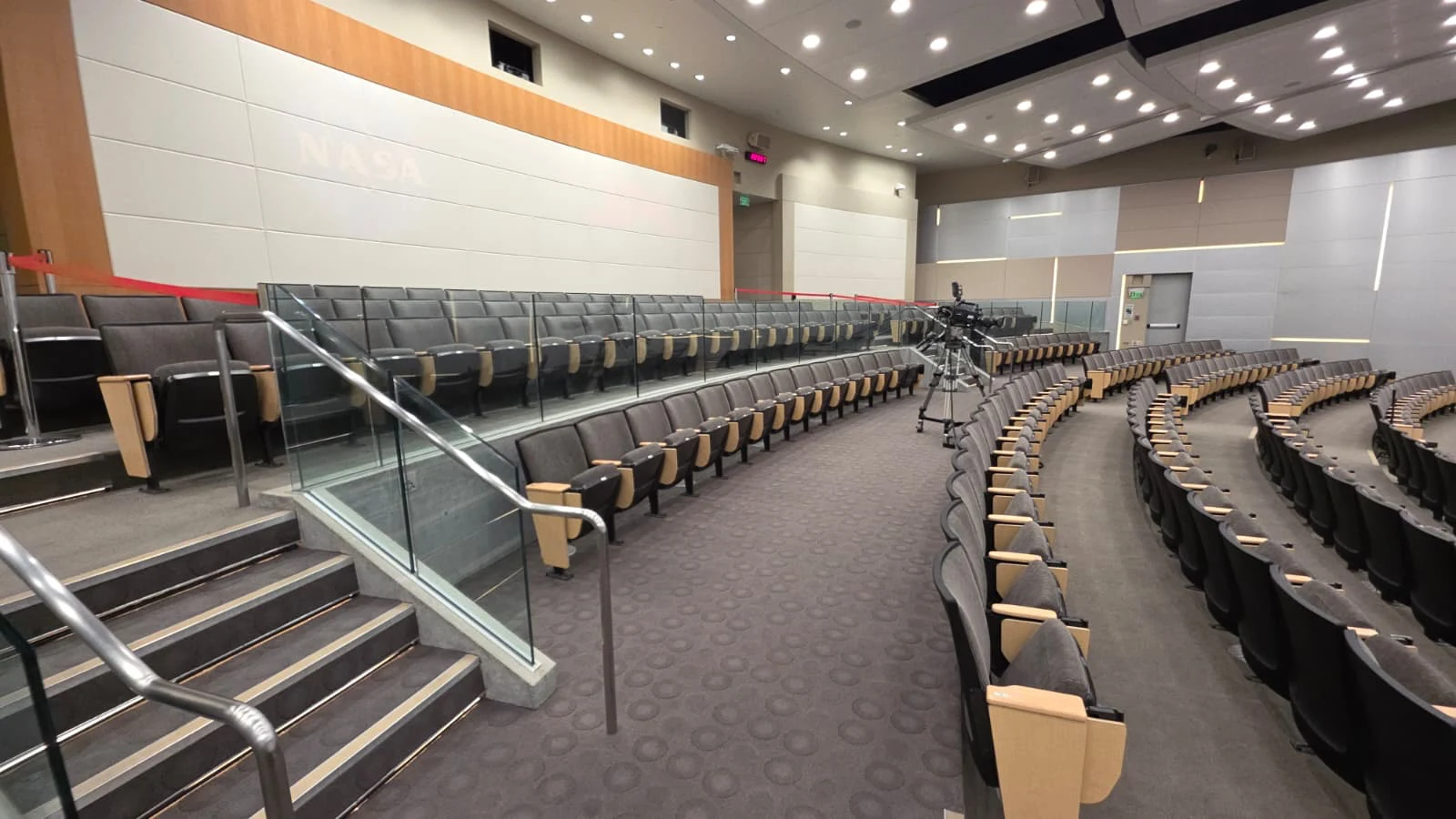 An auditorium with stepped seating, clear glass barriers, and stainless steel handrails beside the stairs.