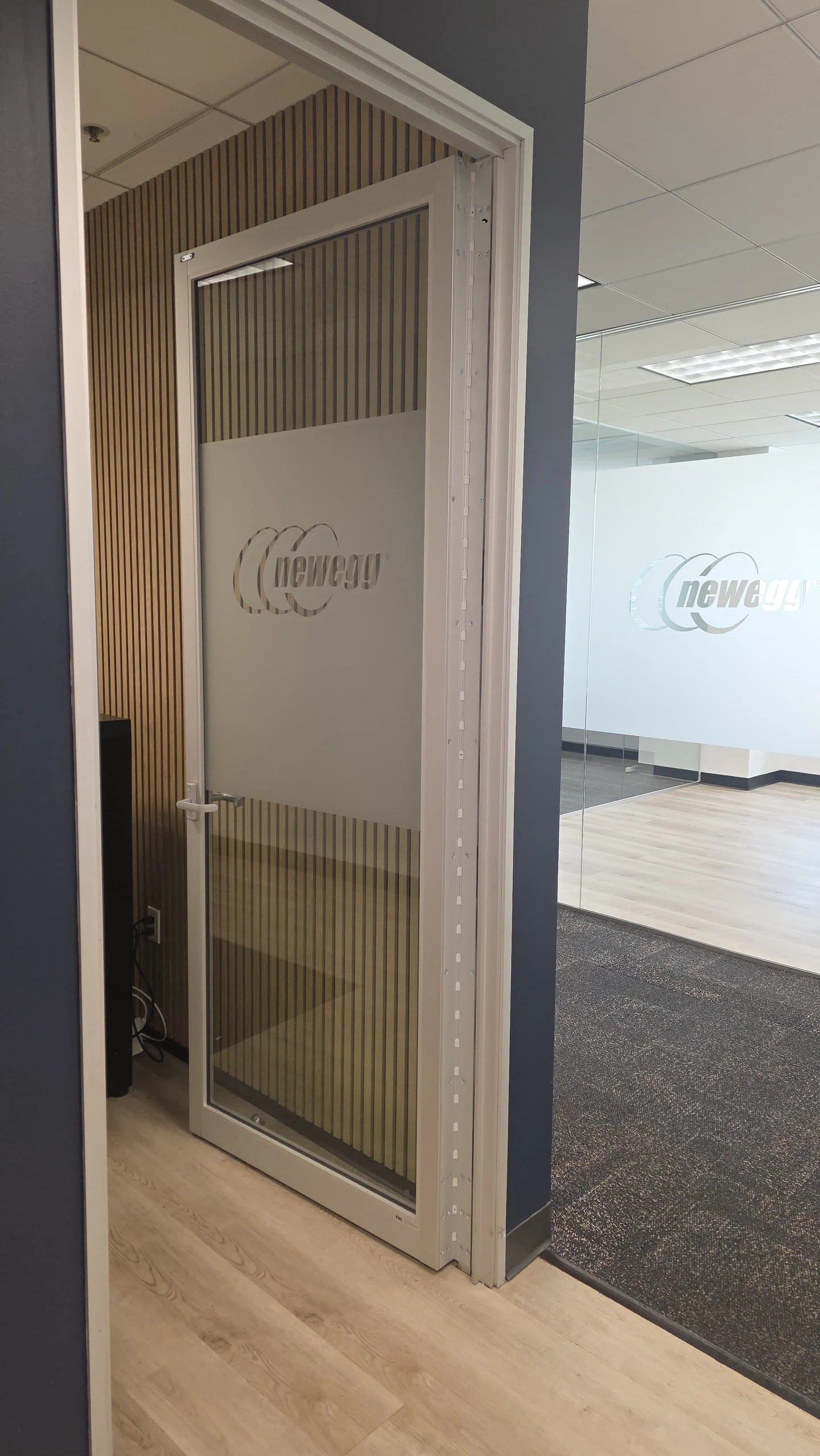 A glass office door with a frosted privacy panel beside a timber slat wall at Newegg.