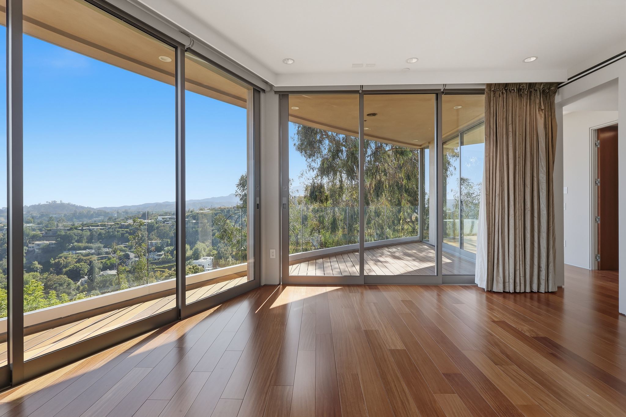 Interior of the Brentwood residence: floor-to-ceiling sliding glass walls opening to a curved terrace and canyon views.