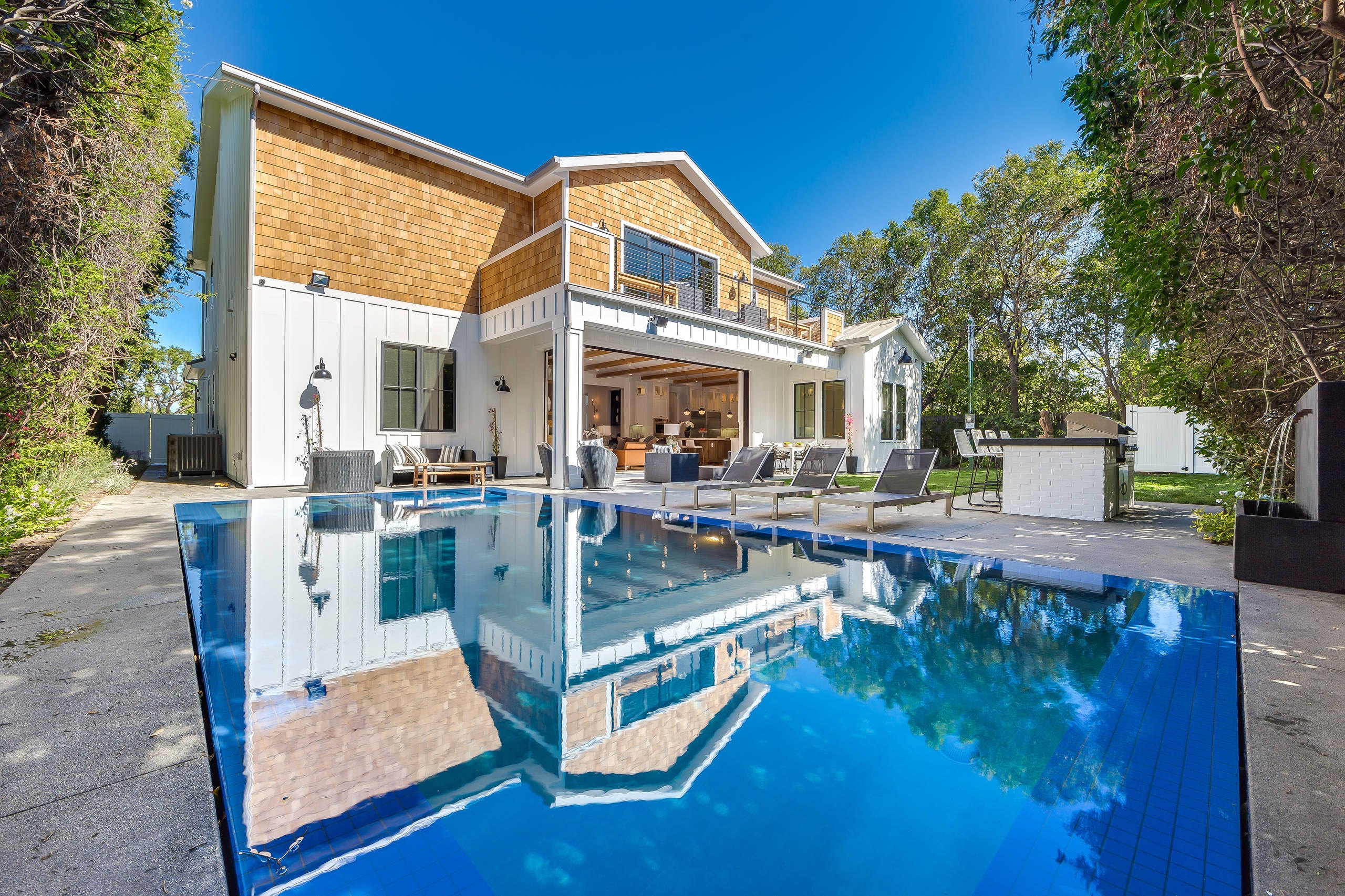 The rear elevation of the Encino farmhouse reflected in its pool at dusk.