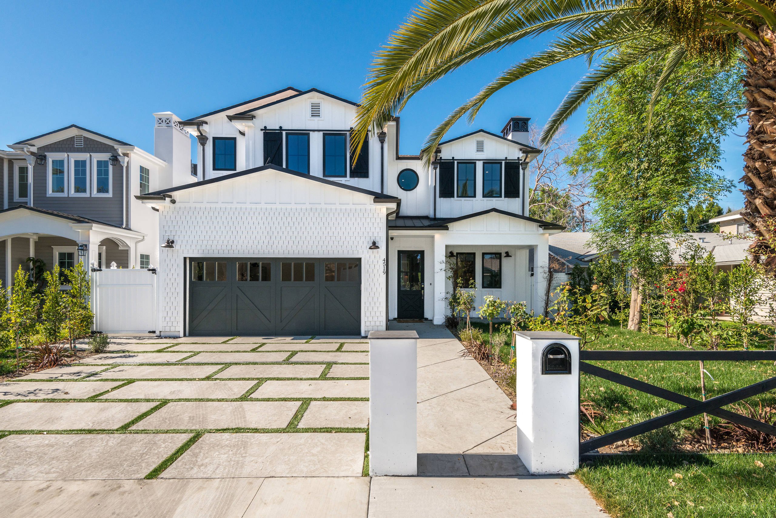 The white board-and-batten front elevation of a Sherman Oaks residence with a dark garage door and a palm.